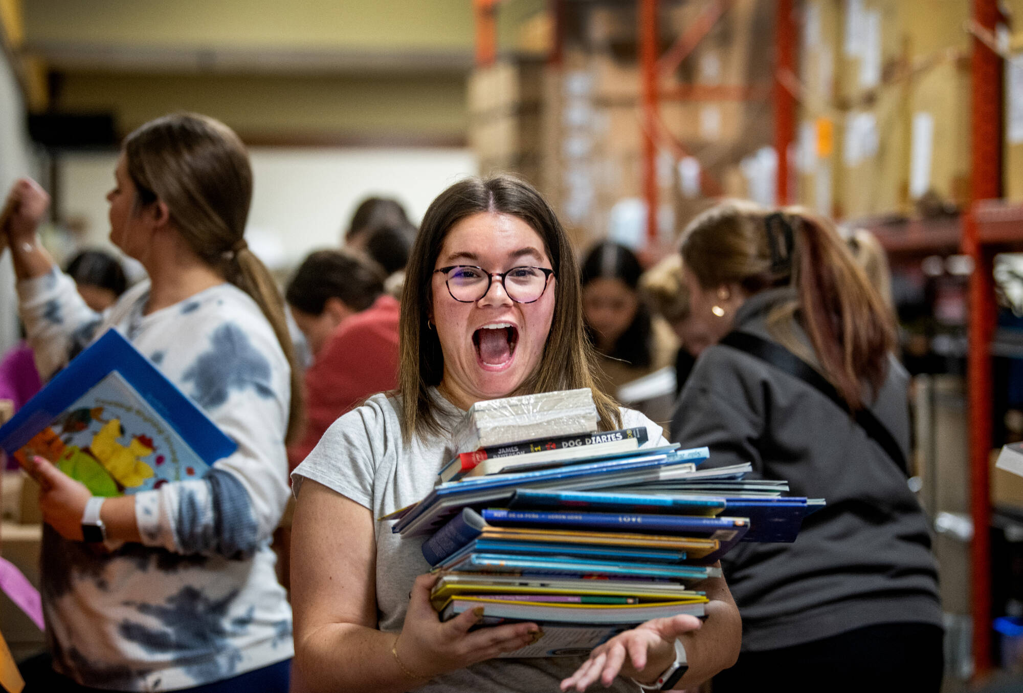 woman smiling widely while holding a stack of children's books